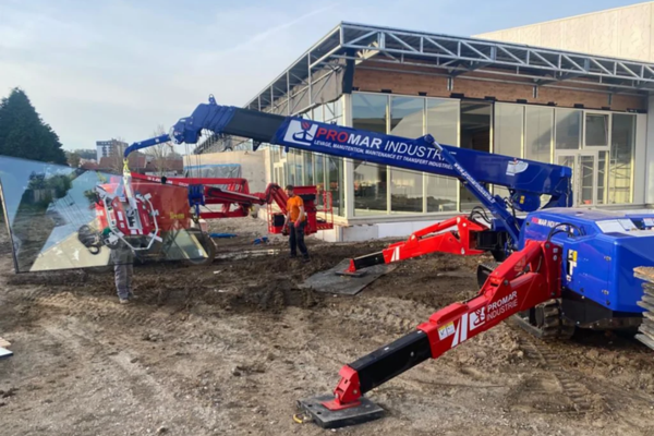 Deux mini-grues rouges et bleues soulèvent du verre sur un chantier. Le logo MAR INDUSTRIAL est visible.