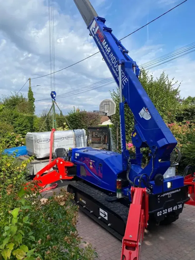 Chantier de construction avec deux mini-grues. Des ouvriers soulèvent des panneaux près d'un bâtiment.