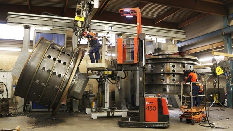 Des ouvriers utilisent des machines dans un atelier pour travailler sur de grands cylindres métalliques.