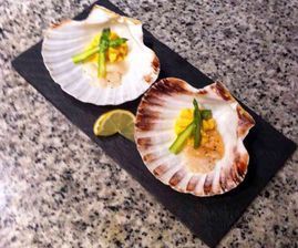 Dos vieiras están sentadas en un plato negro sobre una mesa.