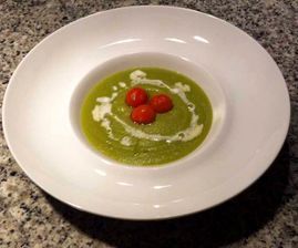 Un tazón de sopa verde con tres tomates encima.