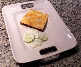 Un plato blanco cubierto con un trozo de comida y rodajas de pepino.