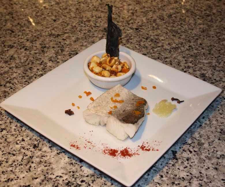 Un plato blanco cubierto con un trozo de pescado y un pequeño tazón de comida.