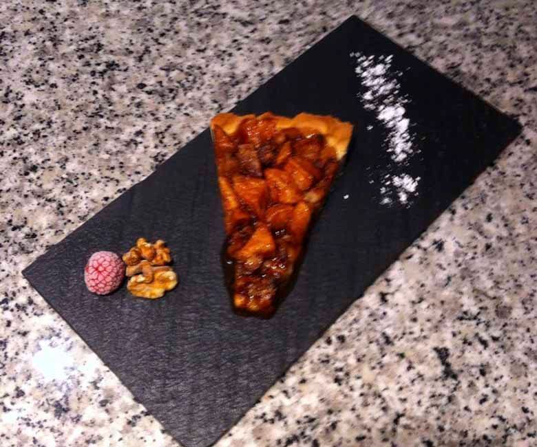 Una rebanada de pastel con nueces y frambuesas en un plato negro