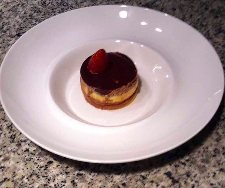 Un postre pequeño con una fresa encima en un plato blanco.