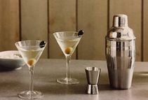 Tres copas de martini con aceitunas y una coctelera sobre una mesa.