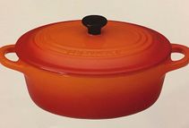 Una olla roja con tapa y asas negras sobre una superficie blanca.