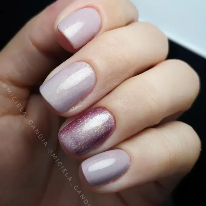 Primer plano de una mano con manicura, con uñas de color rosa pálido y purpurina malva metalizada.