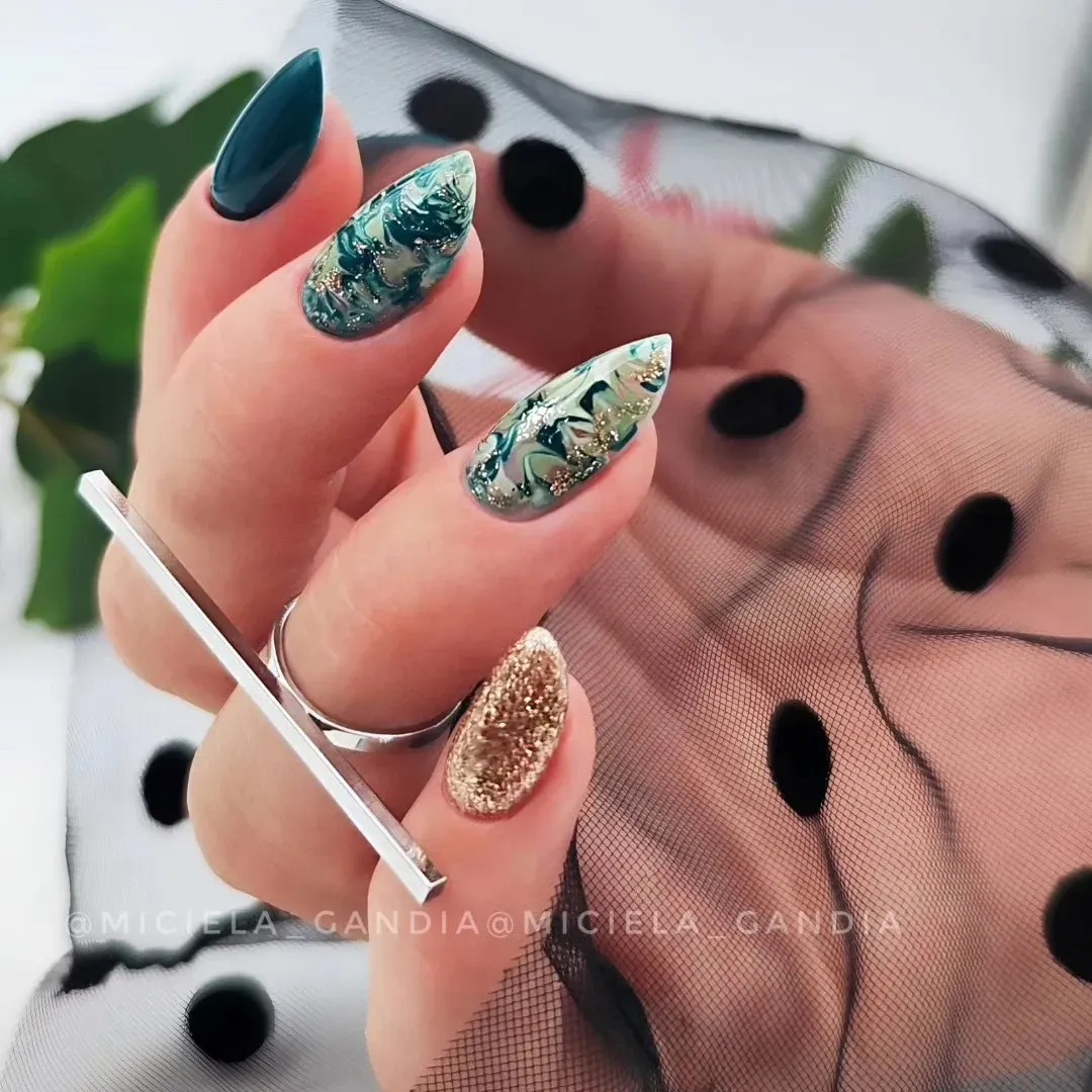 Primer plano de una mano con uñas acrílicas de color turquesa y dorado con purpurina sobre una tela transparente negra de lunares.