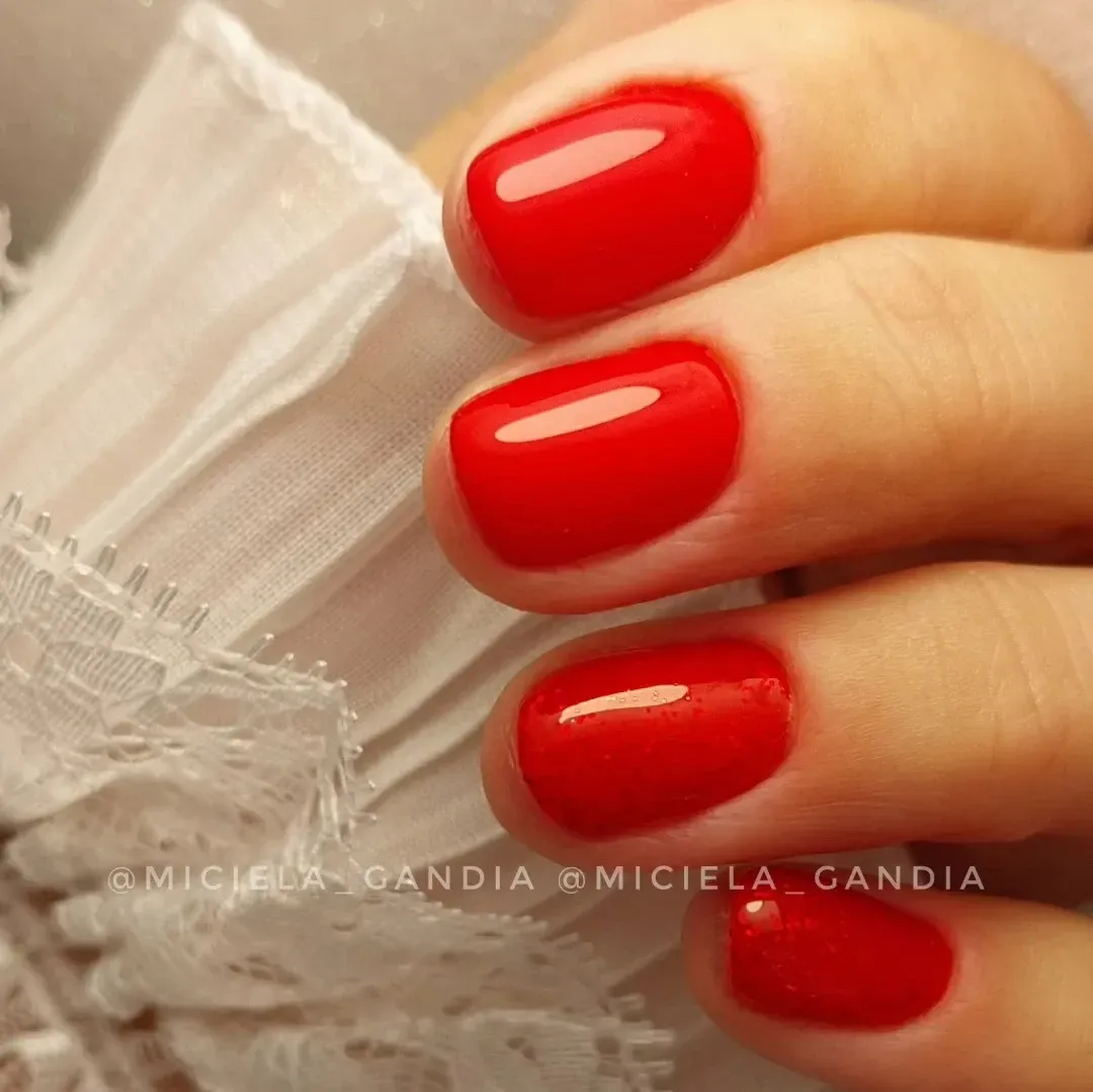 Mano con uñas rojas brillantes y bien cuidadas sosteniendo una tela de encaje blanco.