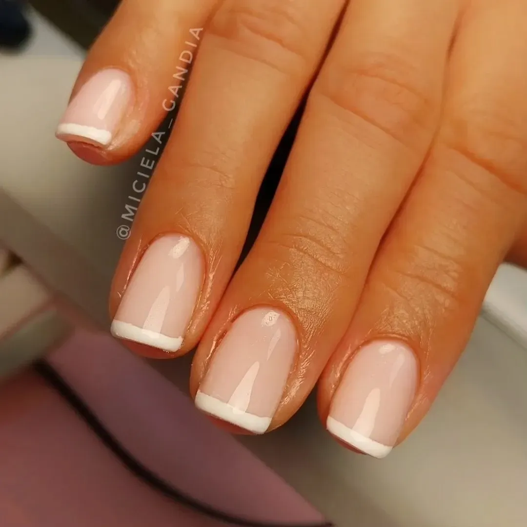 Primer plano de una mano con manicura francesa rosa nude y puntas blancas.