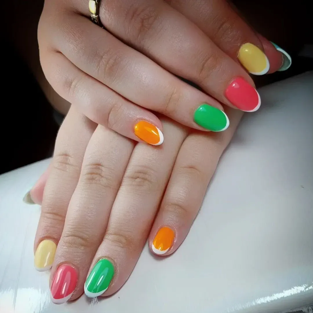 Manos con uñas pintadas de colores brillantes del arcoíris, apoyadas sobre una superficie blanca.