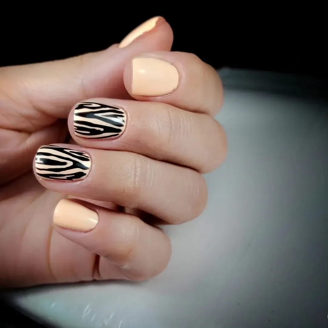Primer plano de una mano con uñas manicuradas en tonos nude y negro con estampado de cebra.
