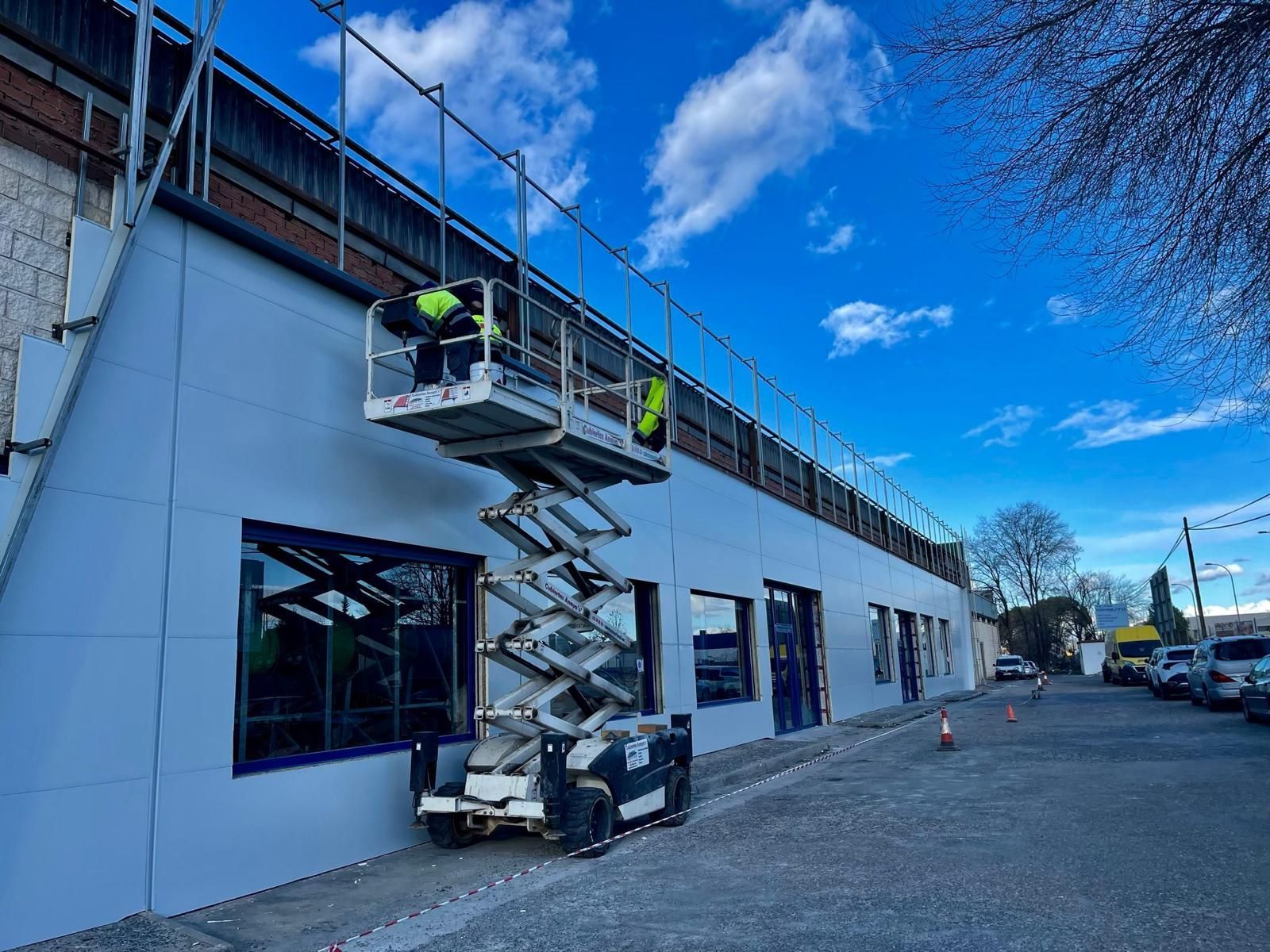 Un hombre está parado en un elevador de tijera al costado de un edificio.