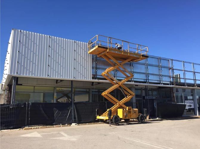 Un elevador de tijera amarillo está estacionado frente a un edificio en construcción.