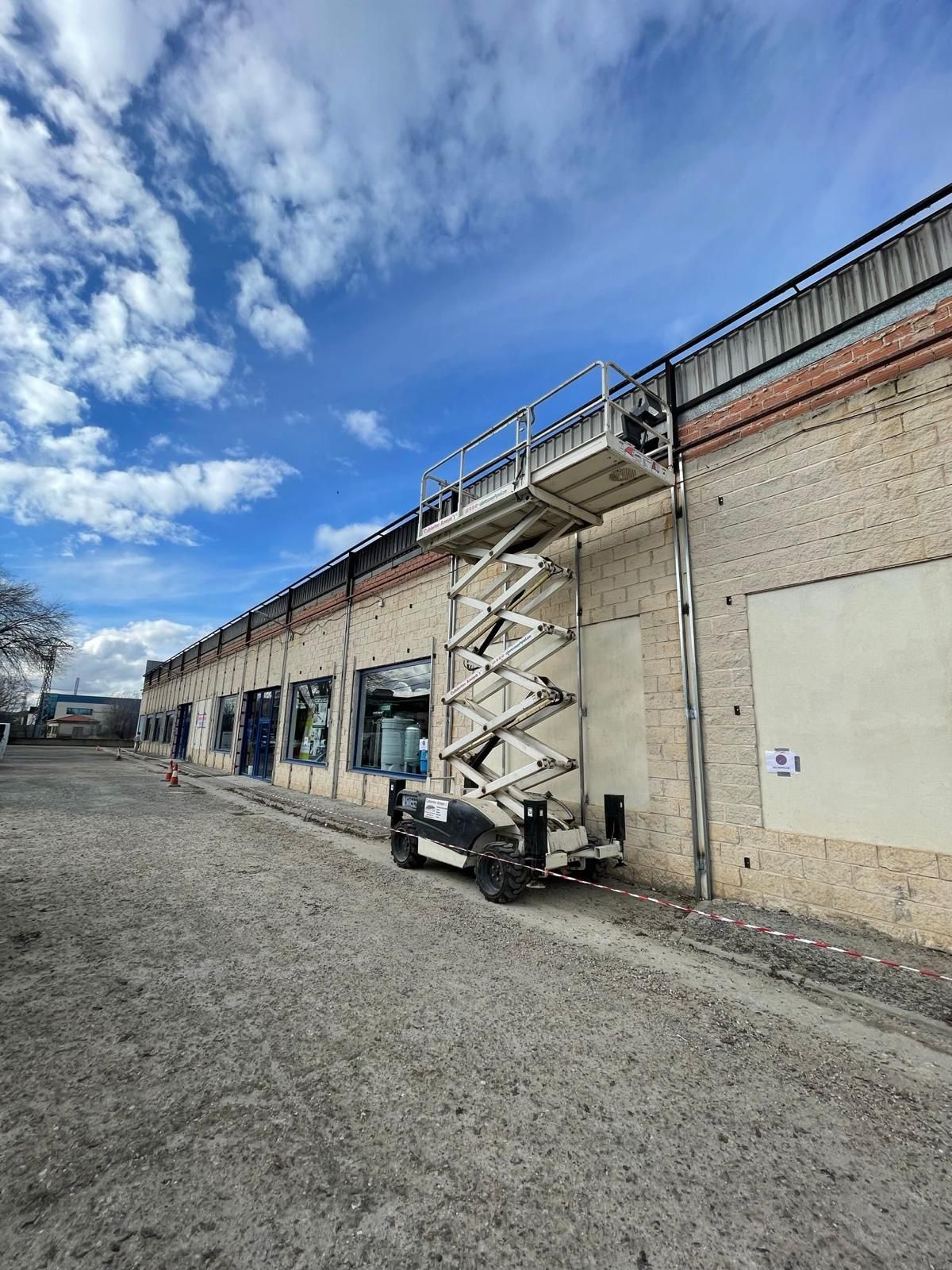 Un elevador de tijera está estacionado frente a un gran edificio de ladrillo.