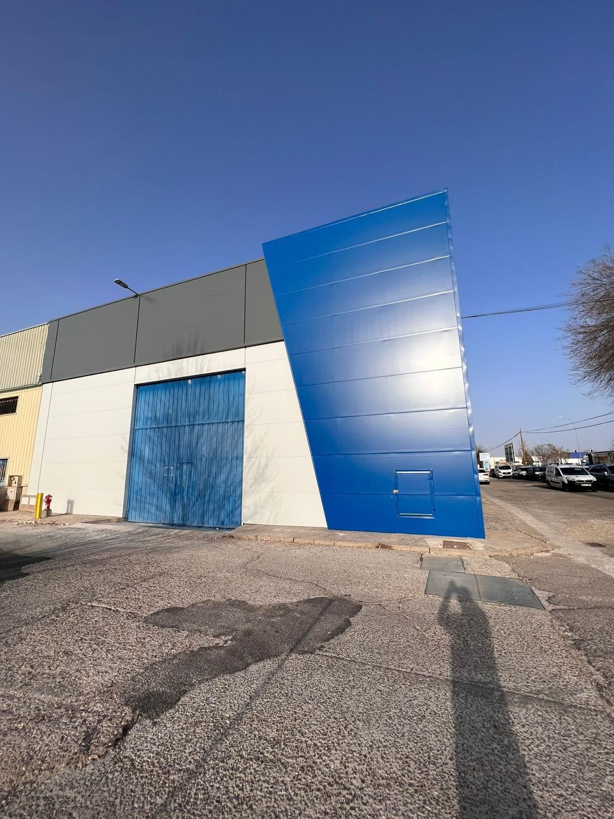 Un edificio azul y blanco con una puerta azul está en un estacionamiento.