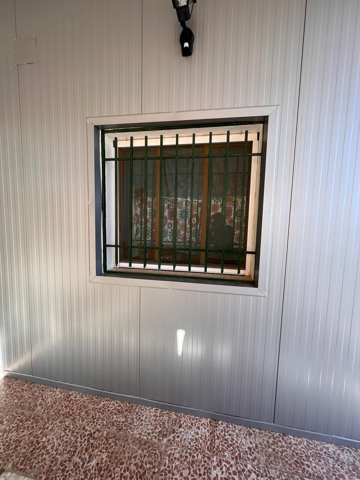 Una pared blanca con una ventana con rejas.