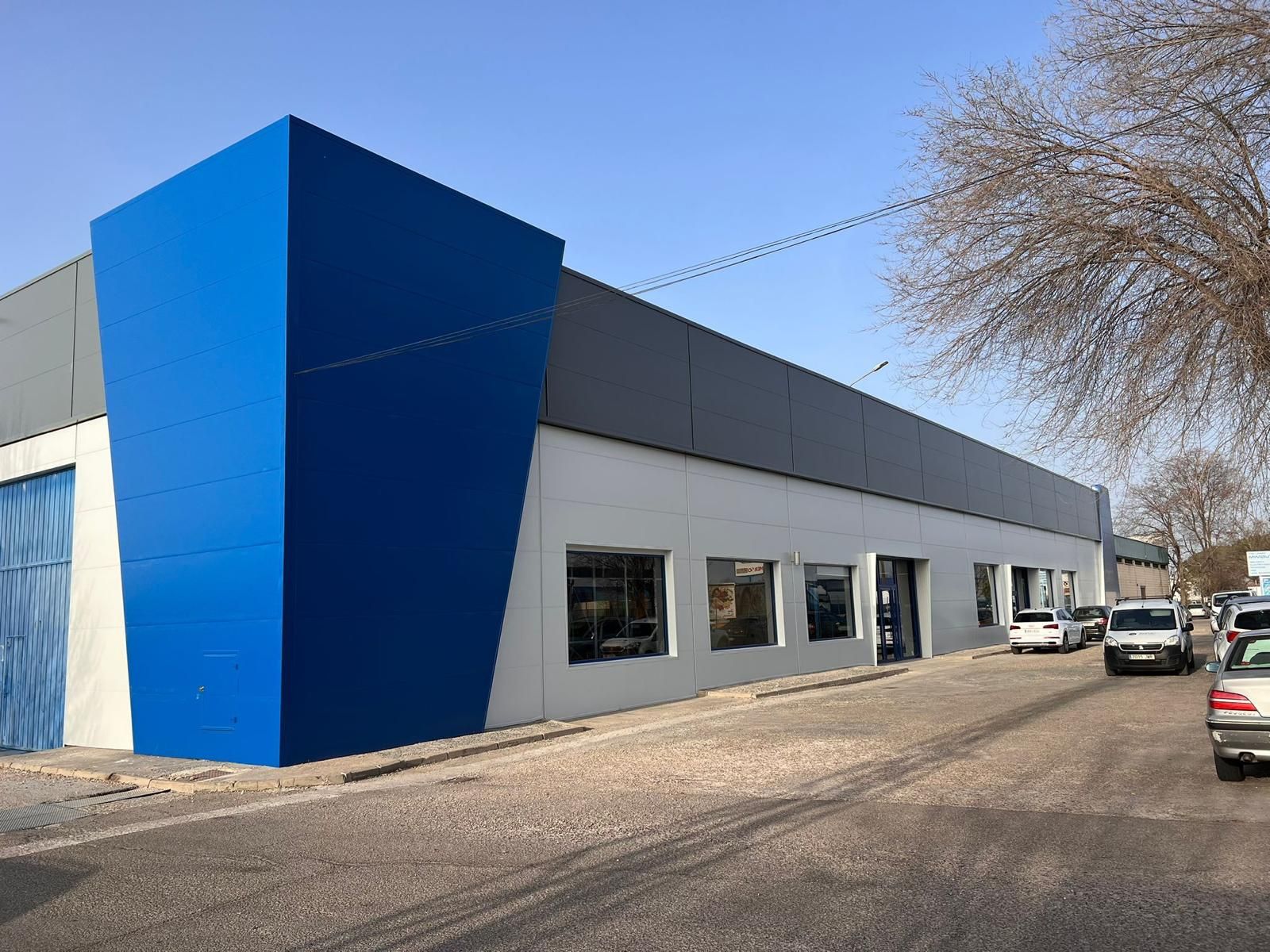 Un edificio azul y blanco con coches aparcados delante.
