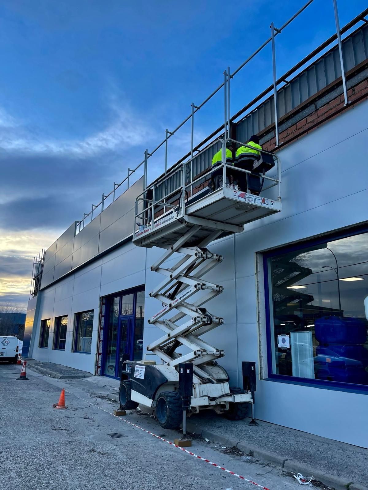 Un hombre está trabajando en el lateral de un edificio en un elevador de tijera.
