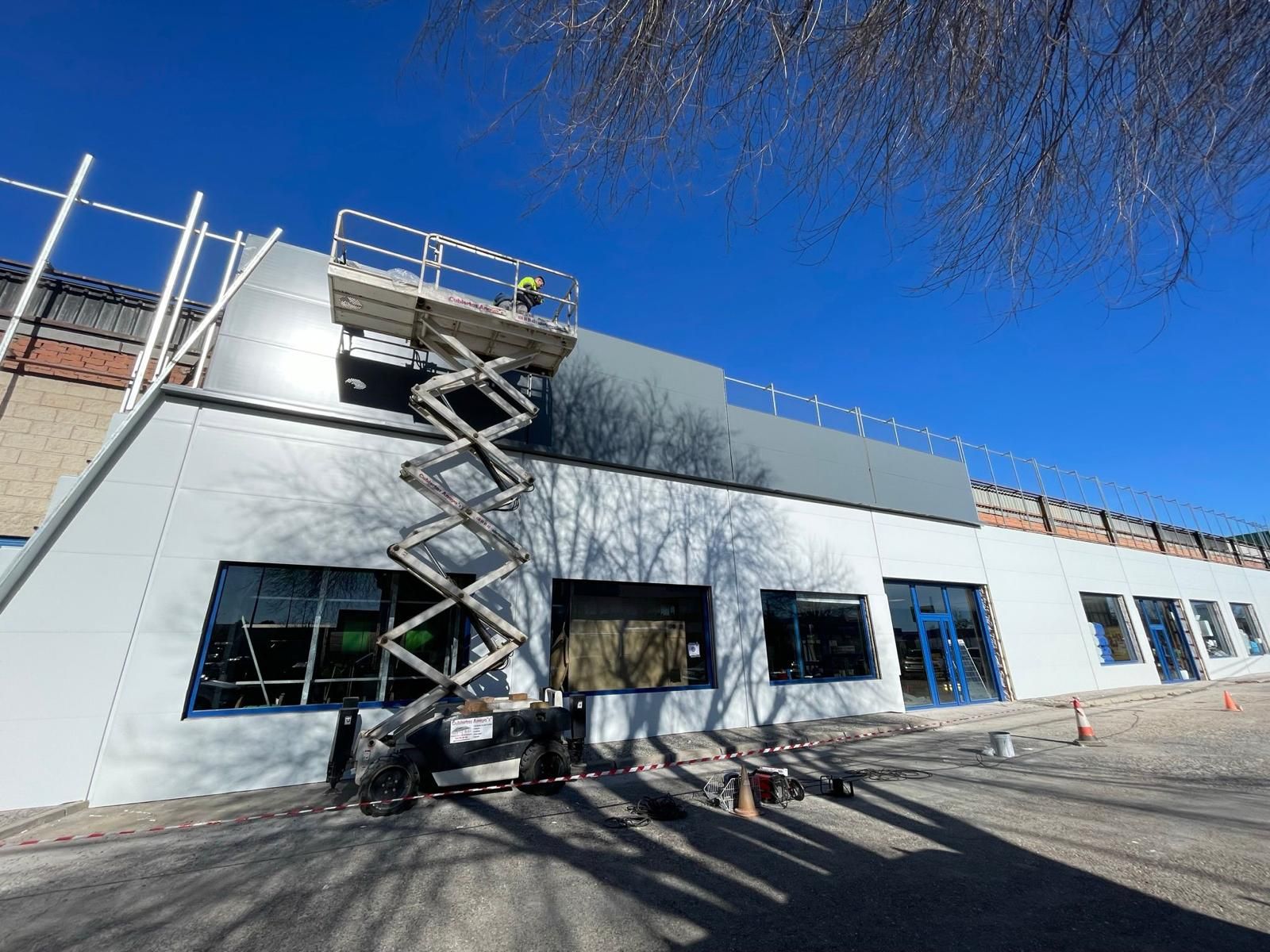 Un hombre está parado en un elevador de tijera al costado de un edificio.