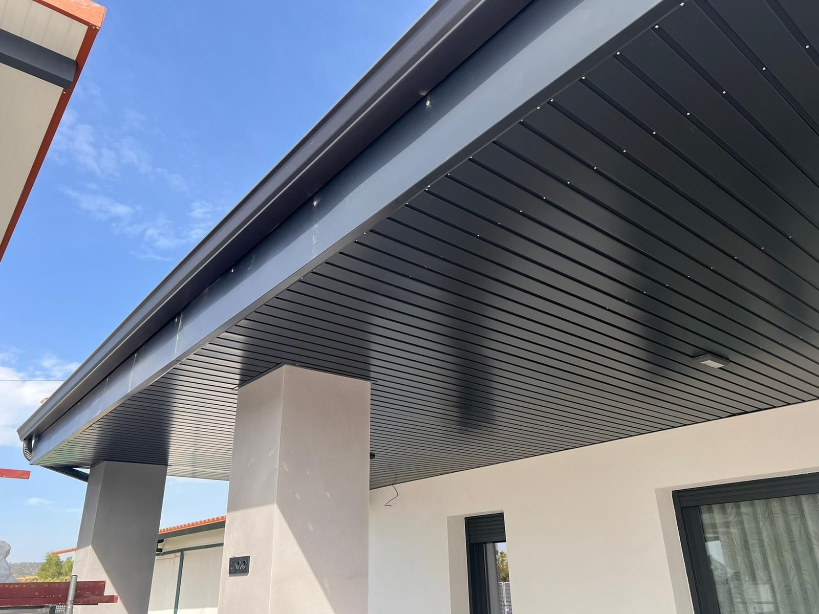 Una casa blanca con un techo negro y un cielo azul al fondo.