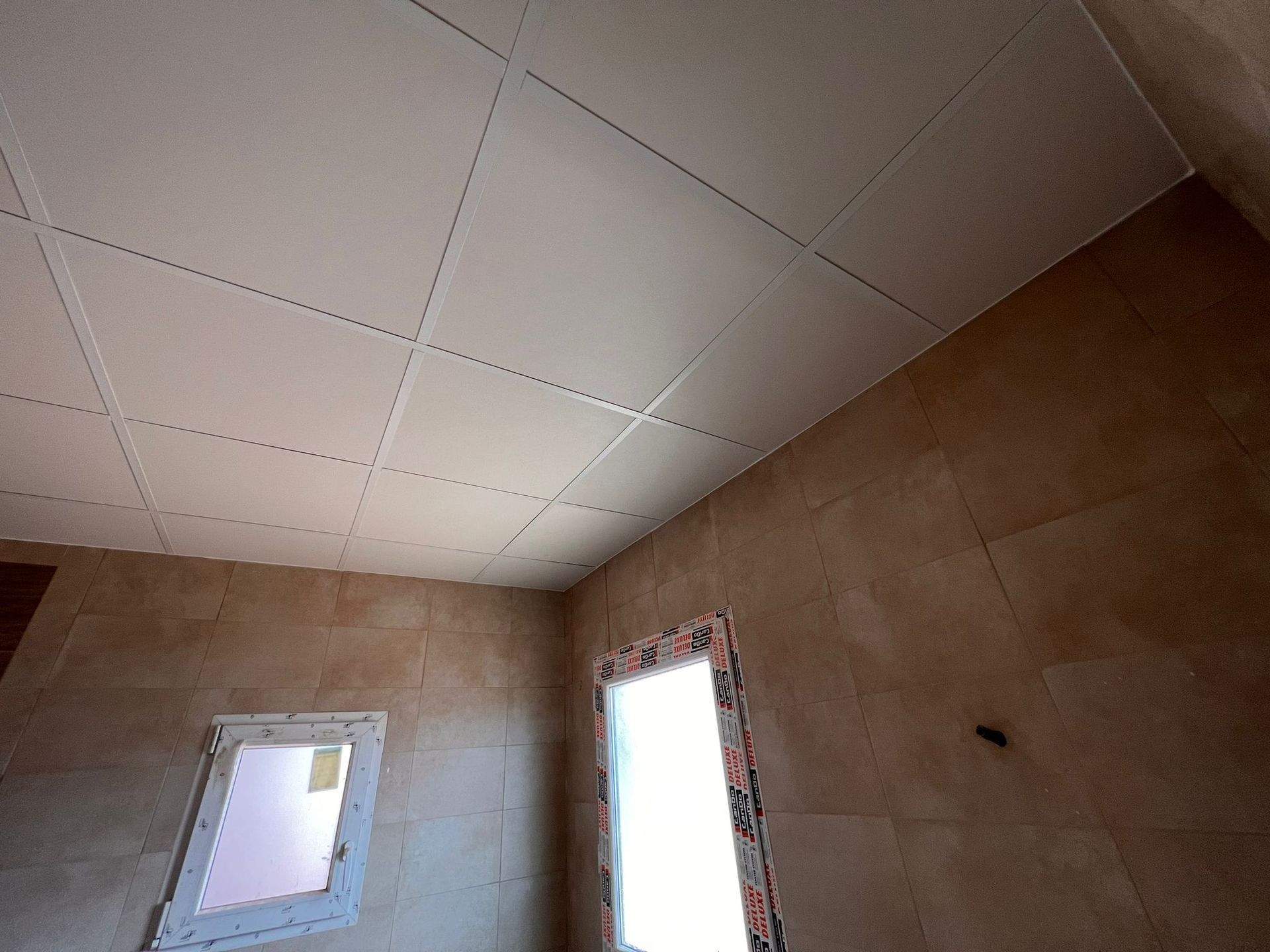 Un baño con techo de azulejos y dos ventanas.