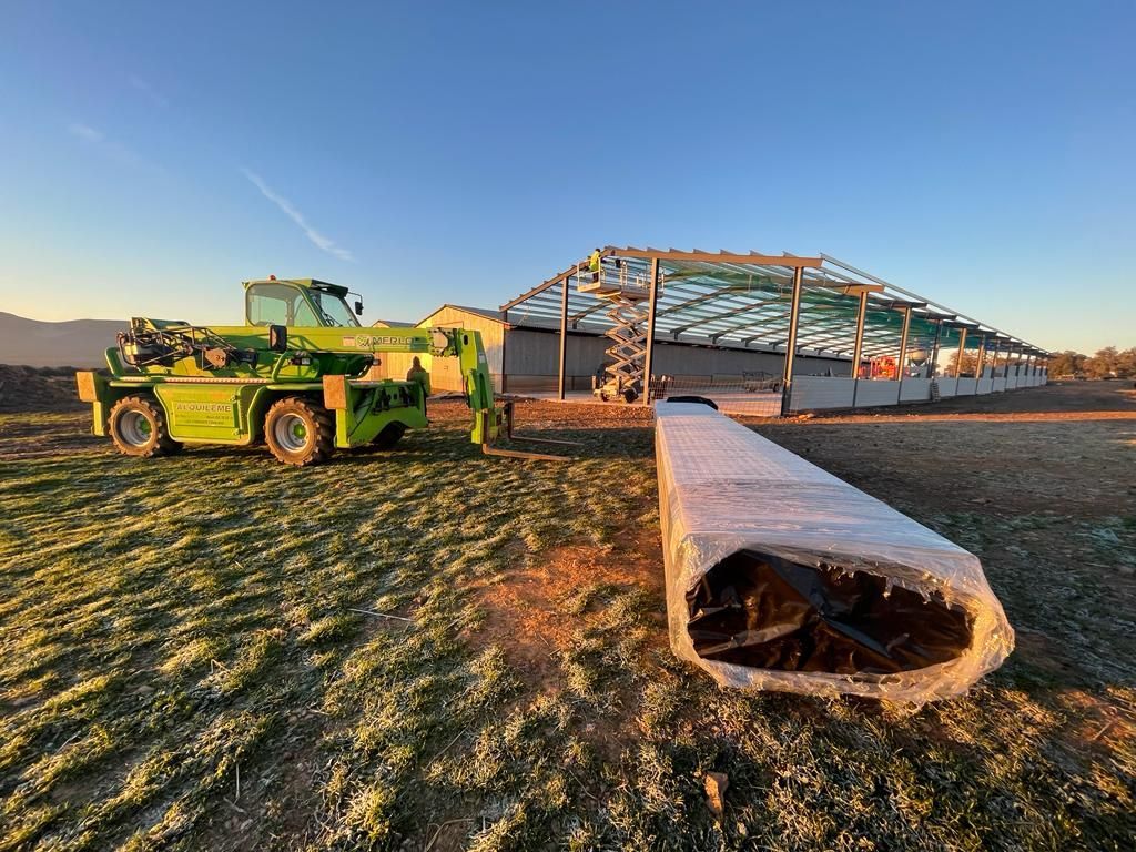 Un camión verde está estacionado en un campo de hierba frente a un edificio en construcción.