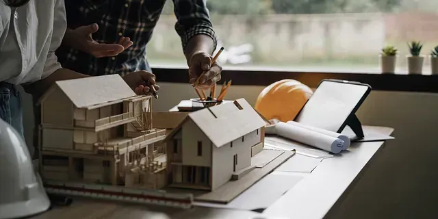 Dos hombres están trabajando en una maqueta de casa sobre una mesa.