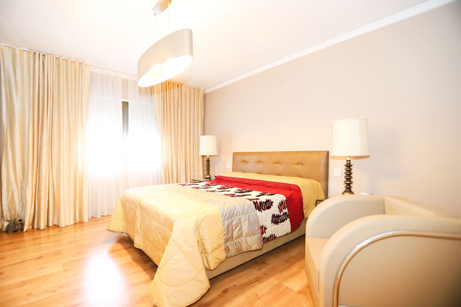 Un dormitorio con una cama, silla, lámparas y cortinas.