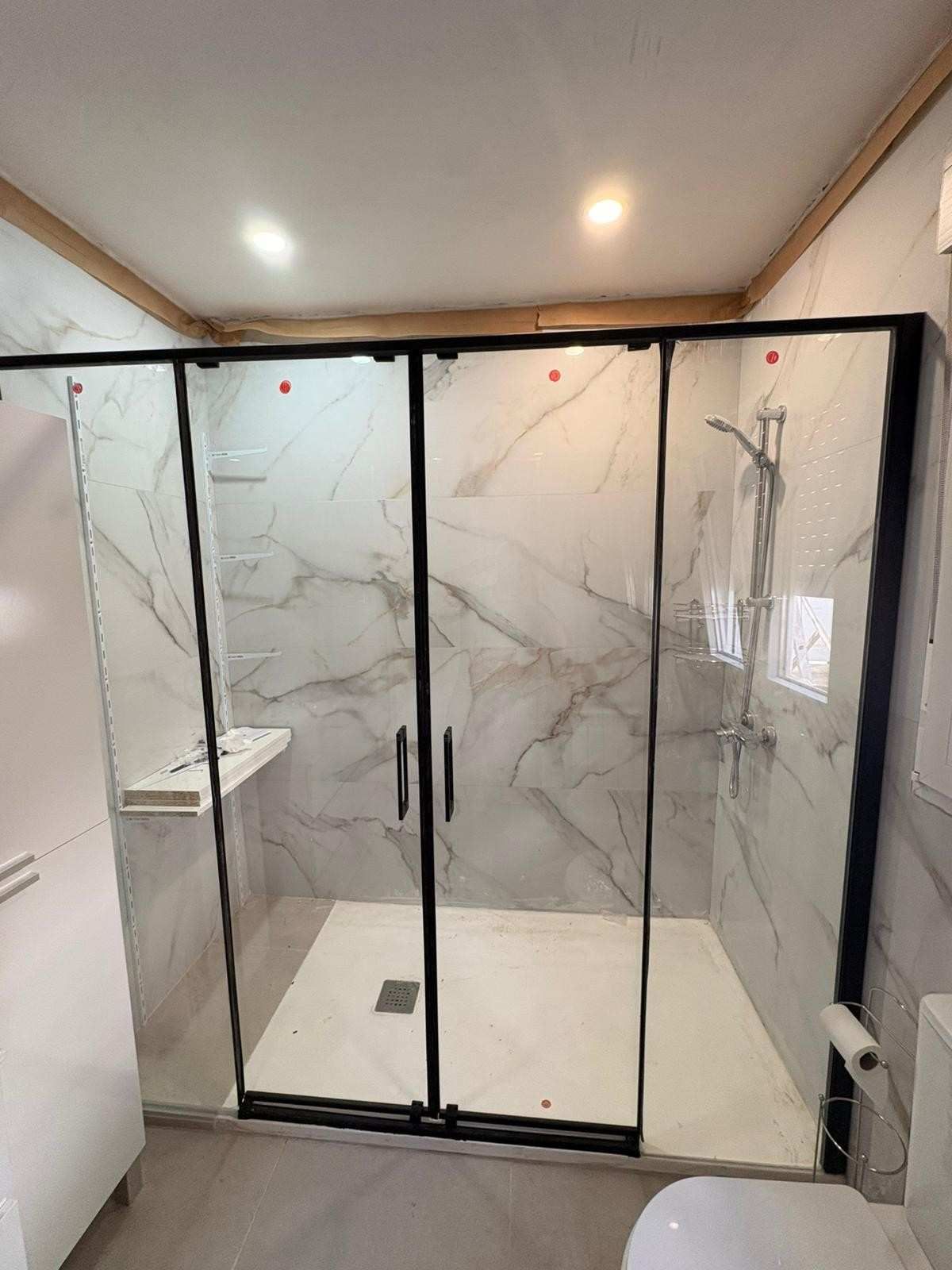 Ducha moderna con puertas de cristal con marco negro y paredes revestidas con azulejos que imitan el mármol.