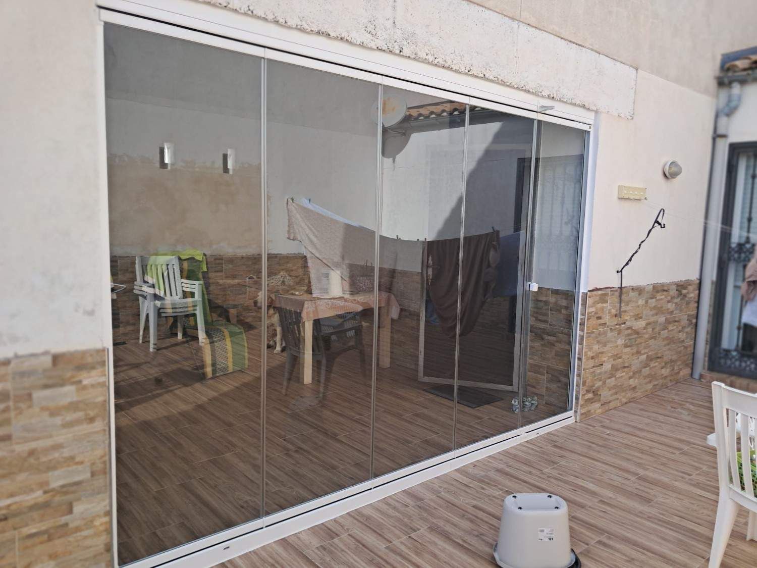 Patio con grandes puertas corredizas de vidrio, piso con apariencia de madera y muebles de exterior visibles desde el interior.