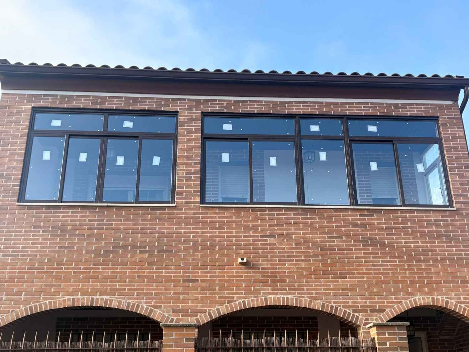 Fachada de ladrillo con grandes ventanas de marcos negros y aberturas arqueadas en la parte inferior.