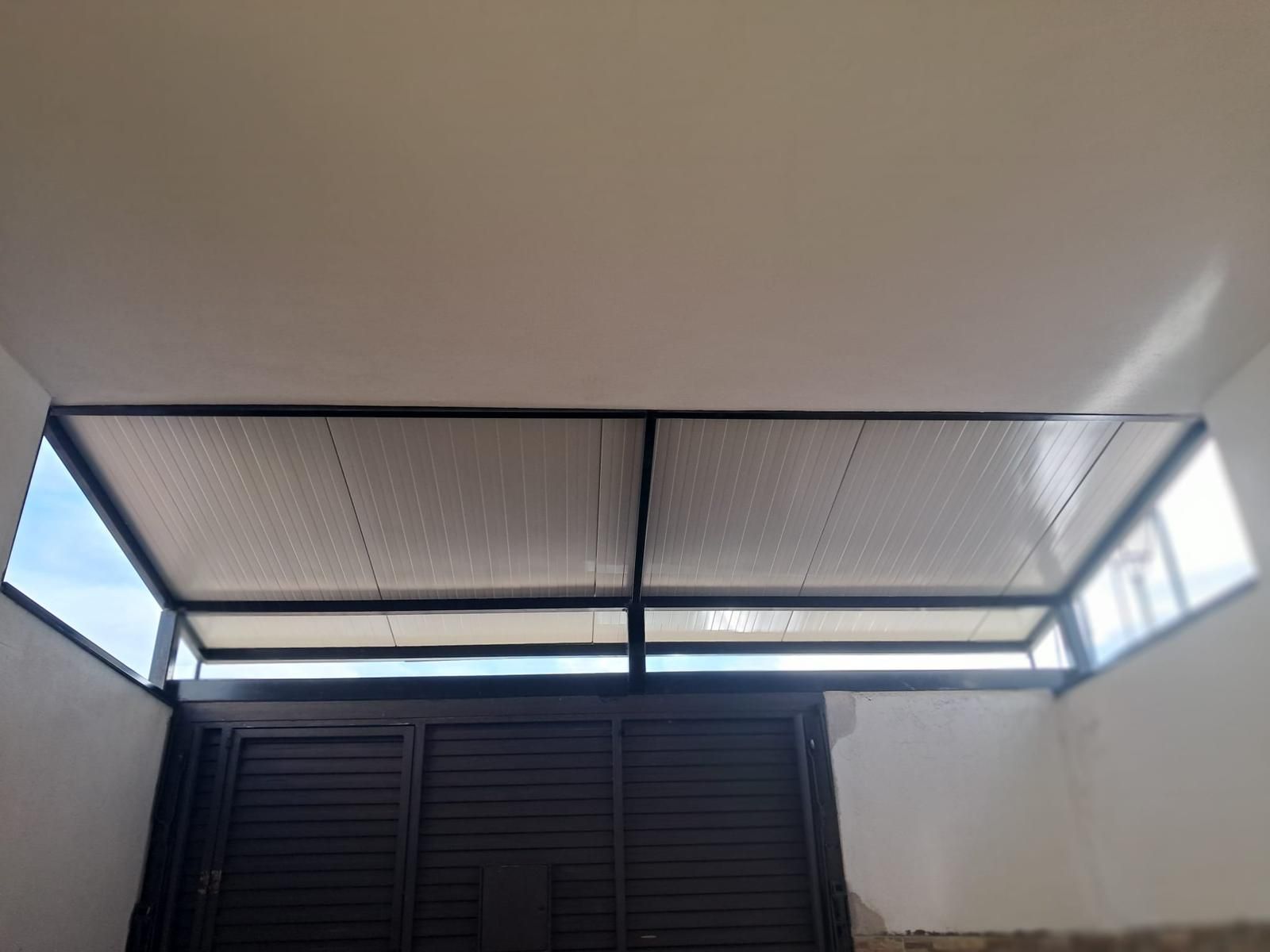 Puerta negra con celosía debajo de una hilera de ventanas abiertas en una pared interior blanca.