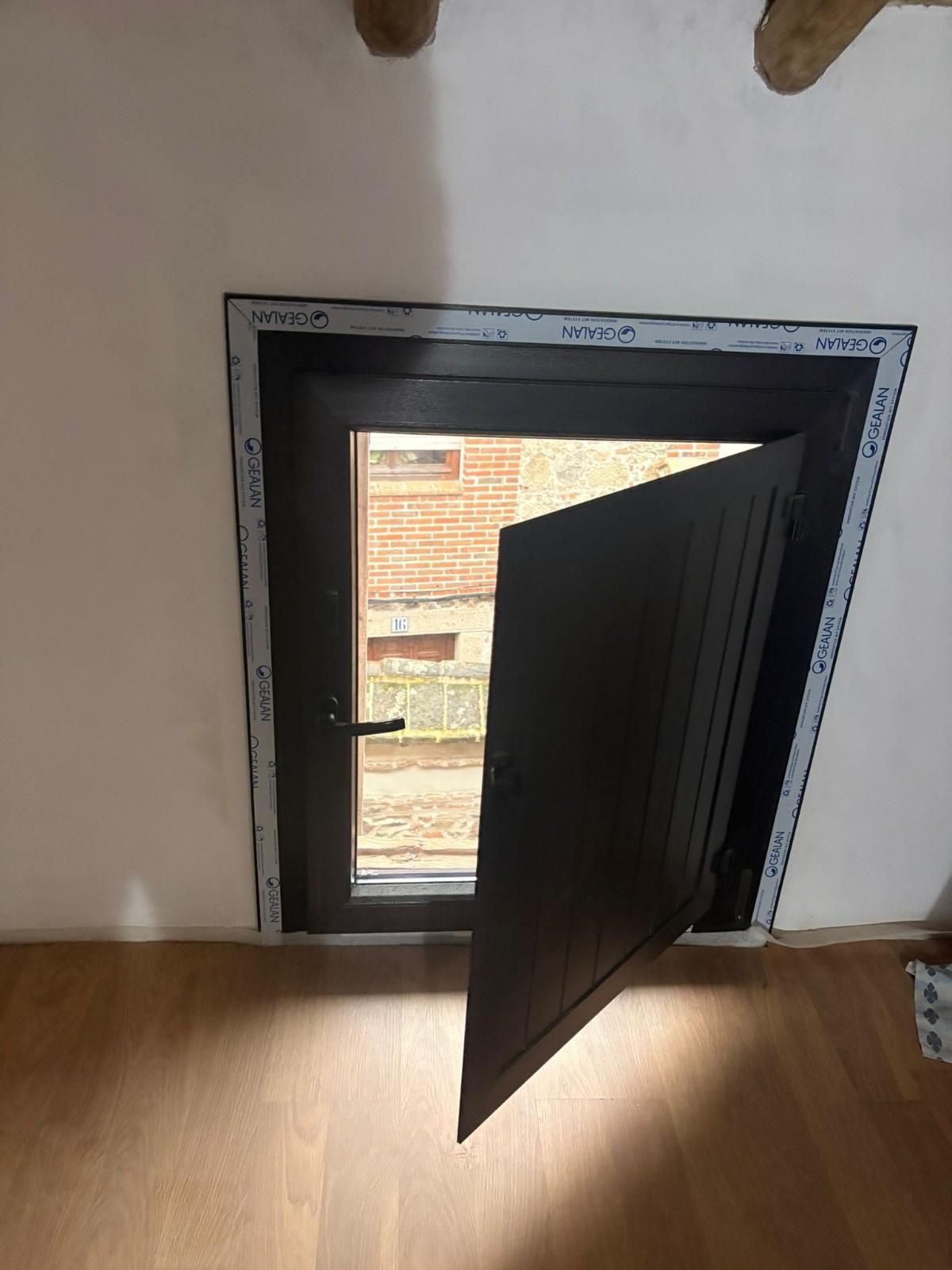 Una puerta negra entreabierta en una habitación de paredes blancas, con la luz del sol entrando a raudales por una ventana.
