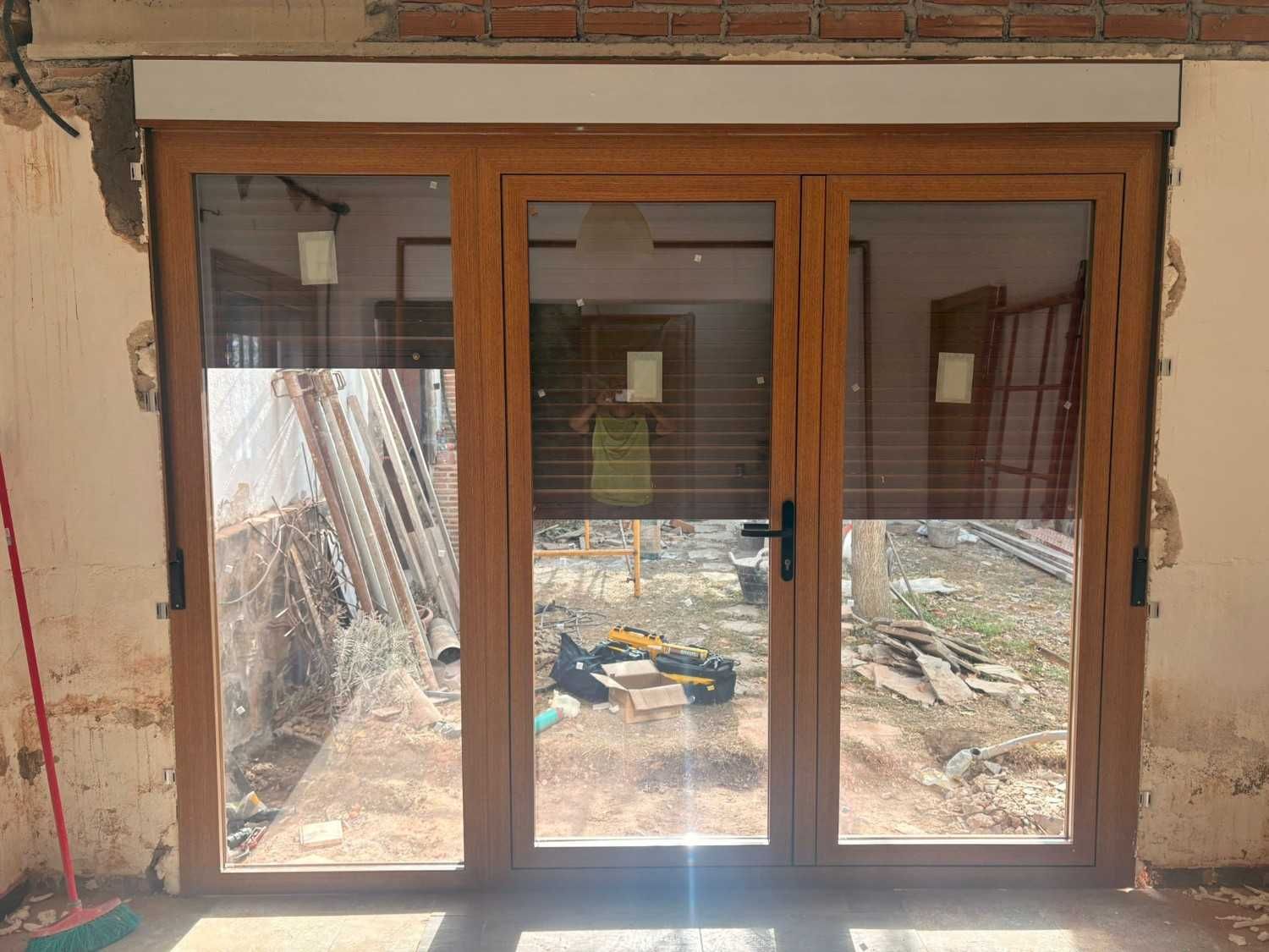 Puertas corredizas de vidrio con marco de madera que dan a un área exterior con persianas y reflejos.