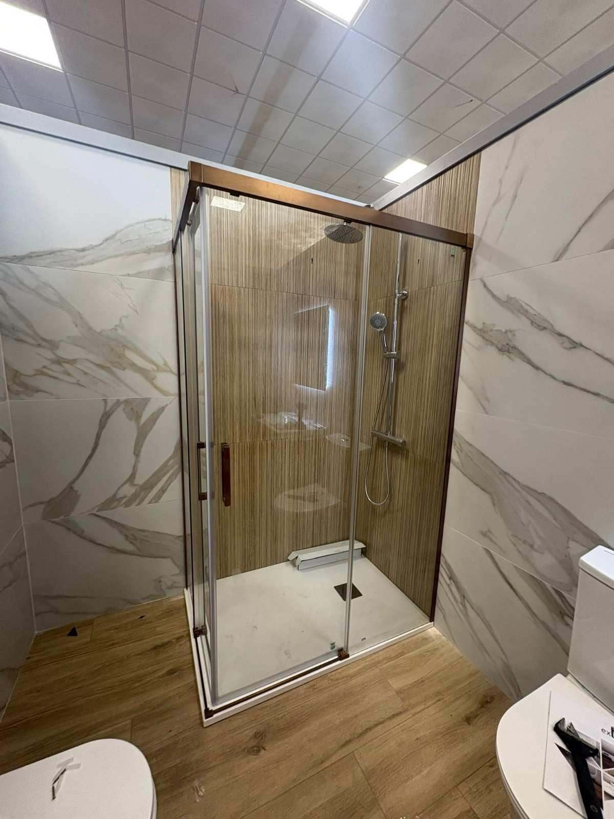 Baño moderno con cabina de ducha de cristal, paredes con aspecto de mármol y baldosas de suelo con aspecto de madera.