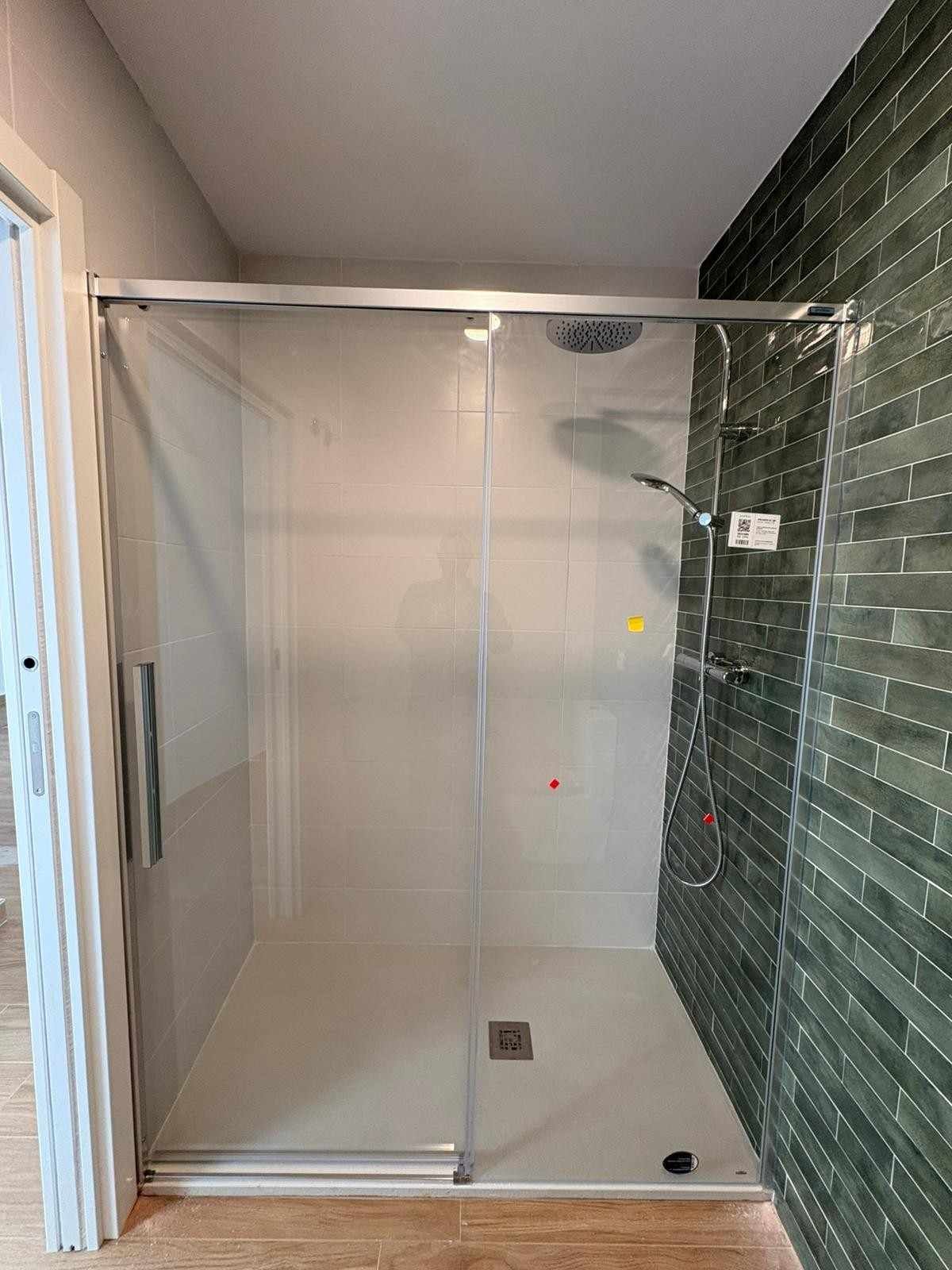 Ducha vacía con azulejos, puerta de cristal y pared decorativa de mosaico verde.