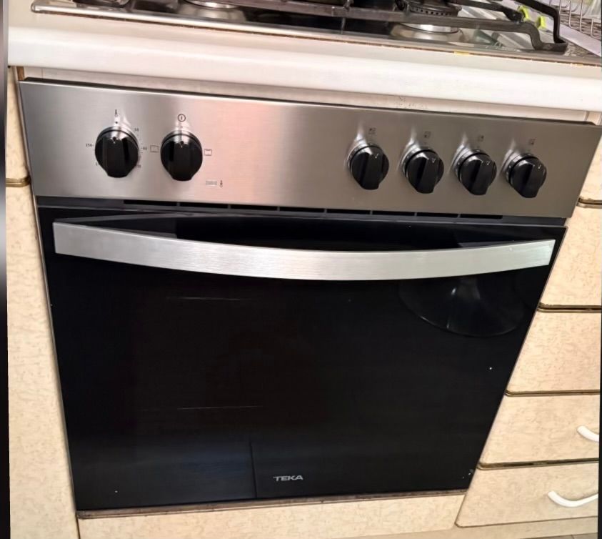 Horno empotrado negro con panel de control de acero inoxidable y cinco perillas, integrado en un mueble de cocina.