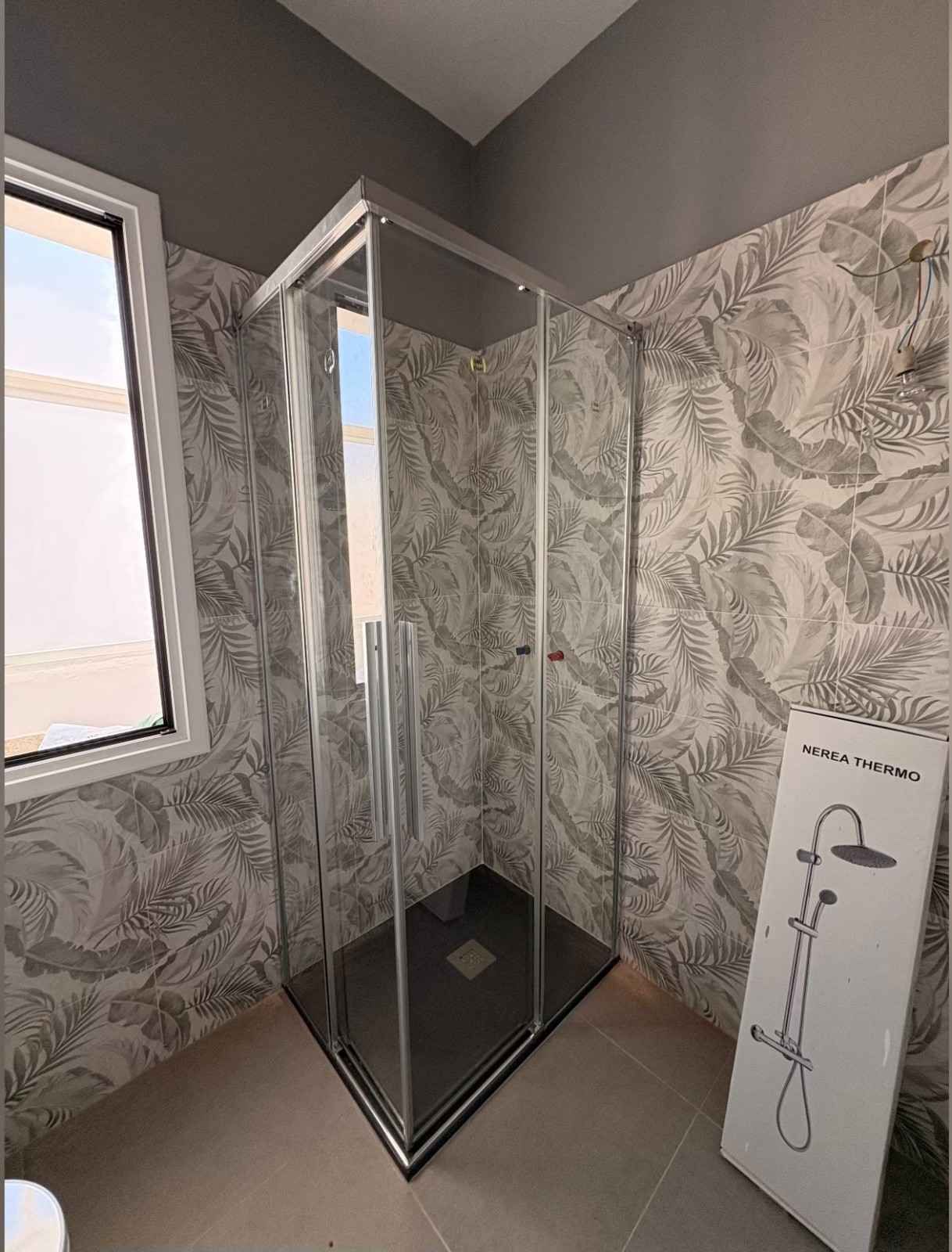 Mampara de ducha de cristal en un baño con papel pintado estampado y panel de ducha mural.