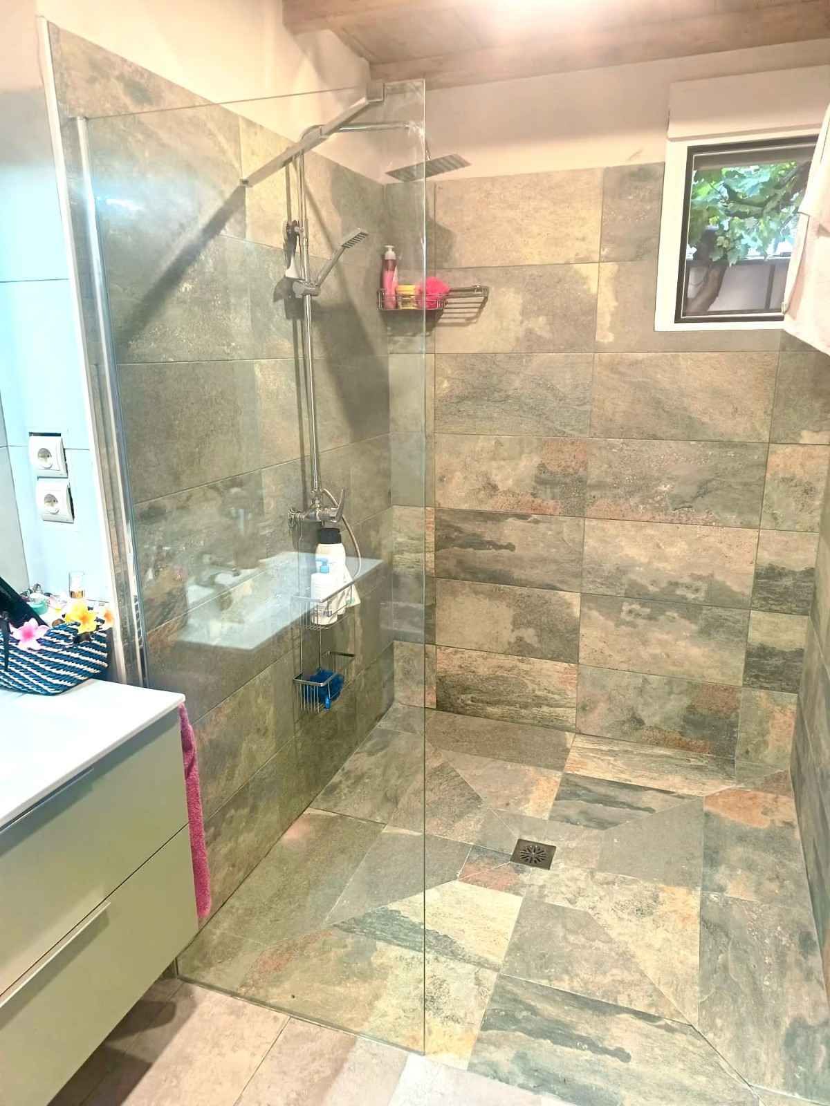 Baño moderno alicatado con cabina de ducha de cristal, paredes con aspecto de piedra y una pequeña ventana.