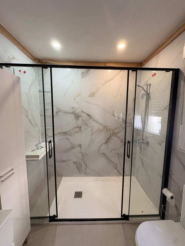Ducha moderna con puertas de cristal, azulejos con estampado de mármol y suelo blanco en un baño.