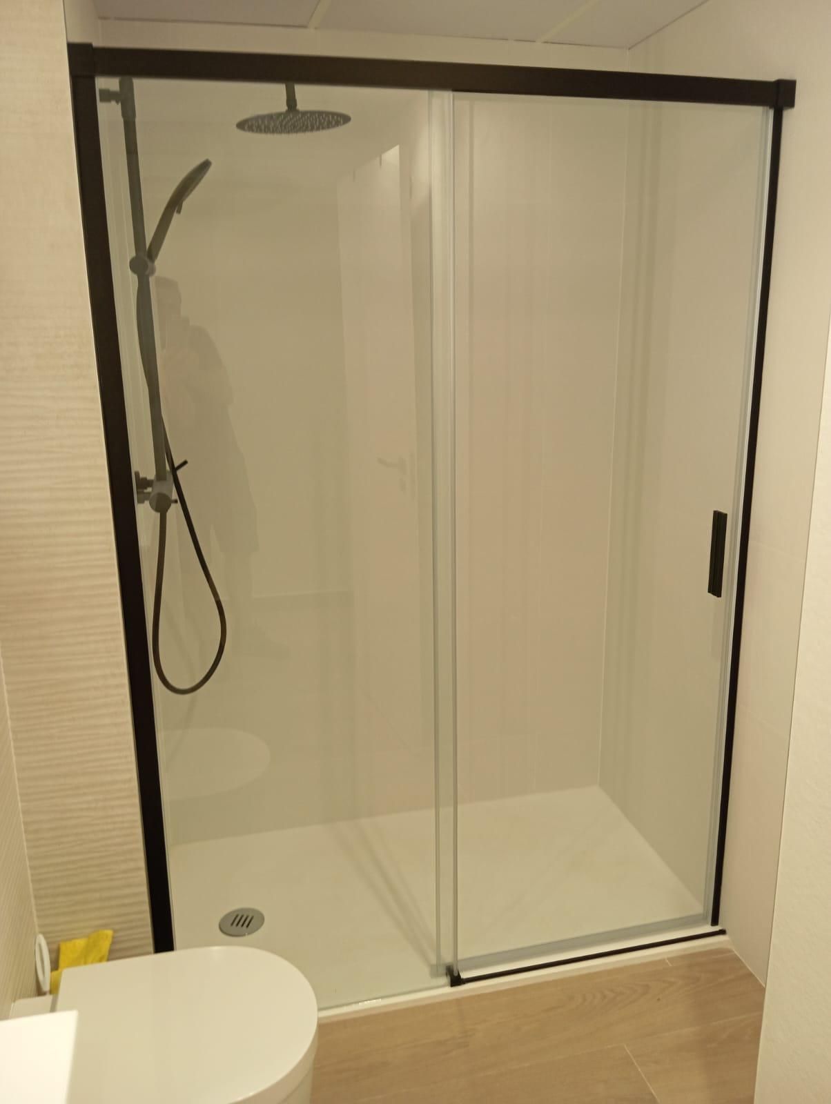 Cabina de ducha de cristal con marco negro y cabezal de ducha de mano en un baño alicatado.