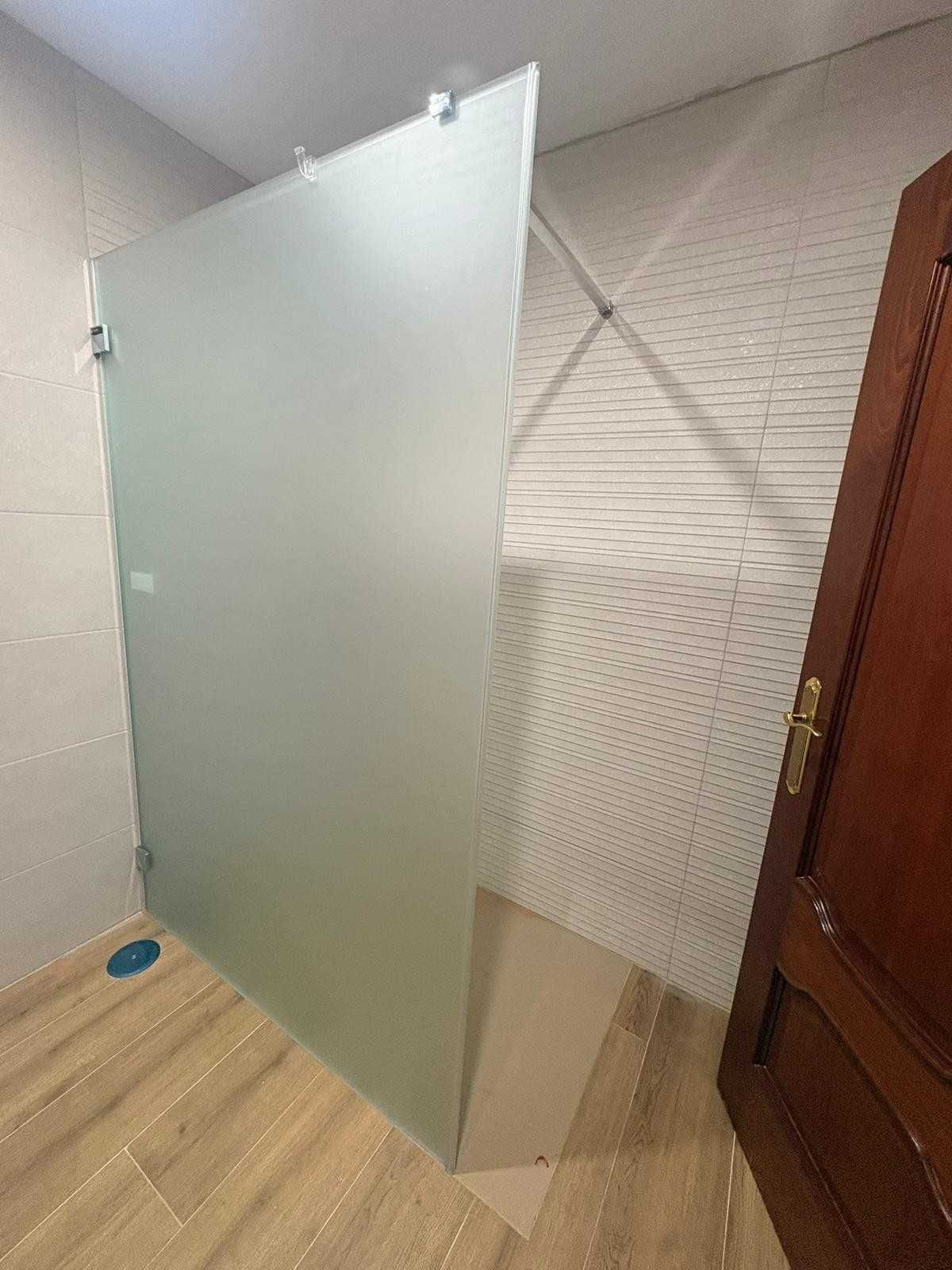 Panel de ducha de vidrio esmerilado junto a una puerta de madera en un baño alicatado.