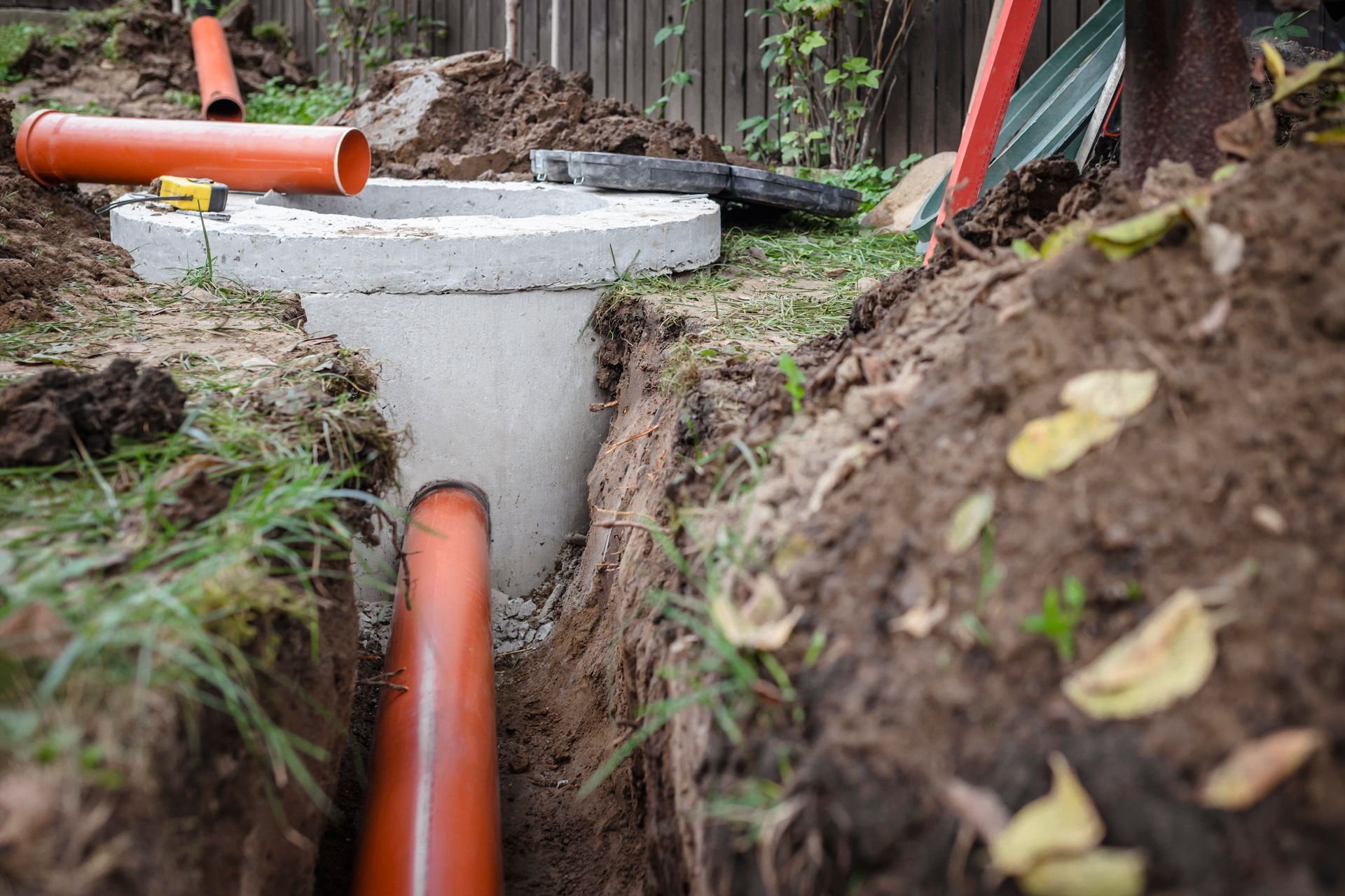Installation de tuyaux orange raccordés à un puits en béton creusé dans une cour gazonnée.