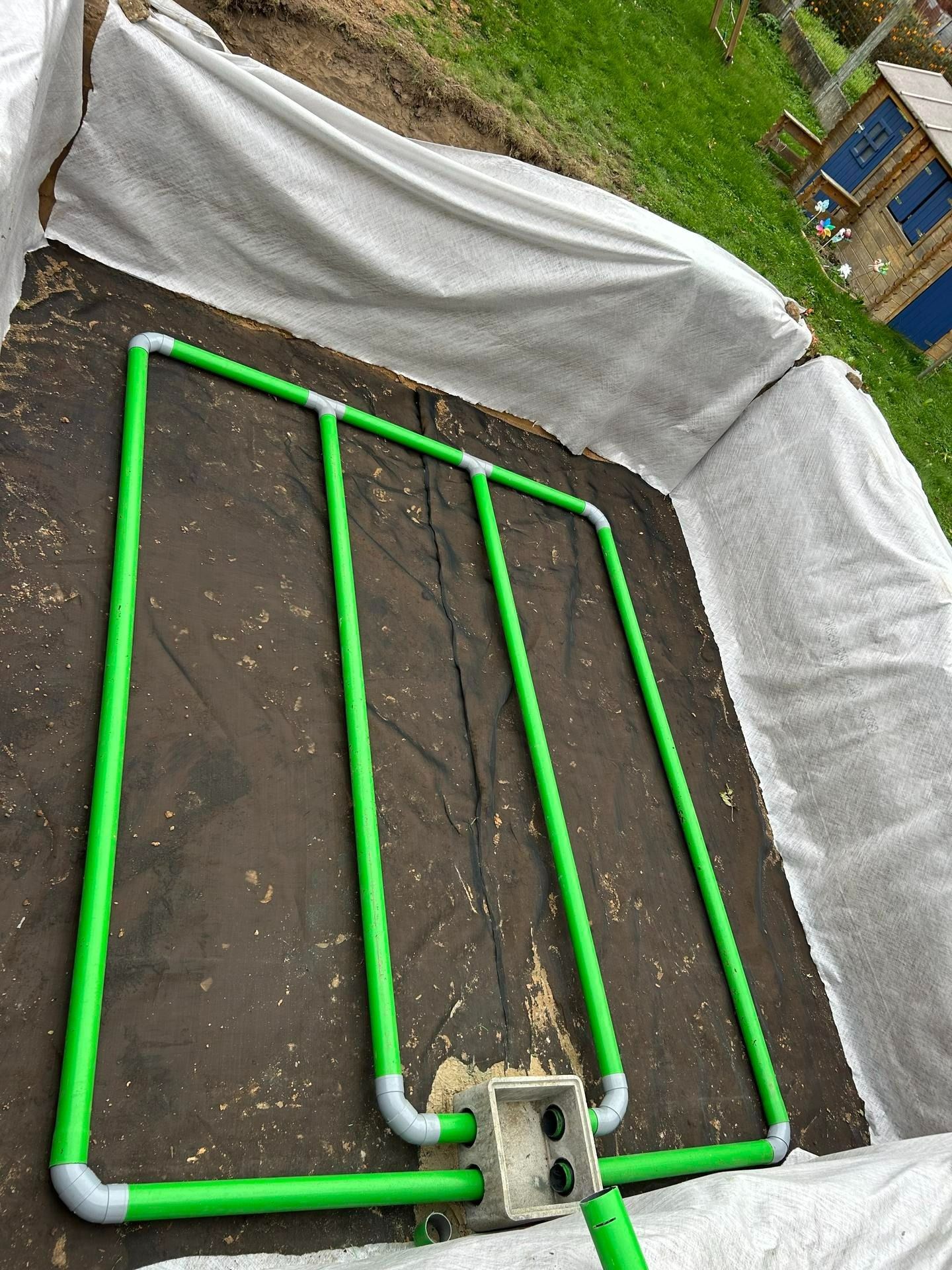 Système composé de tuyaux en PVC vert posés sur un sol sombre, sous une toile blanche, dans un parterre de jardin.