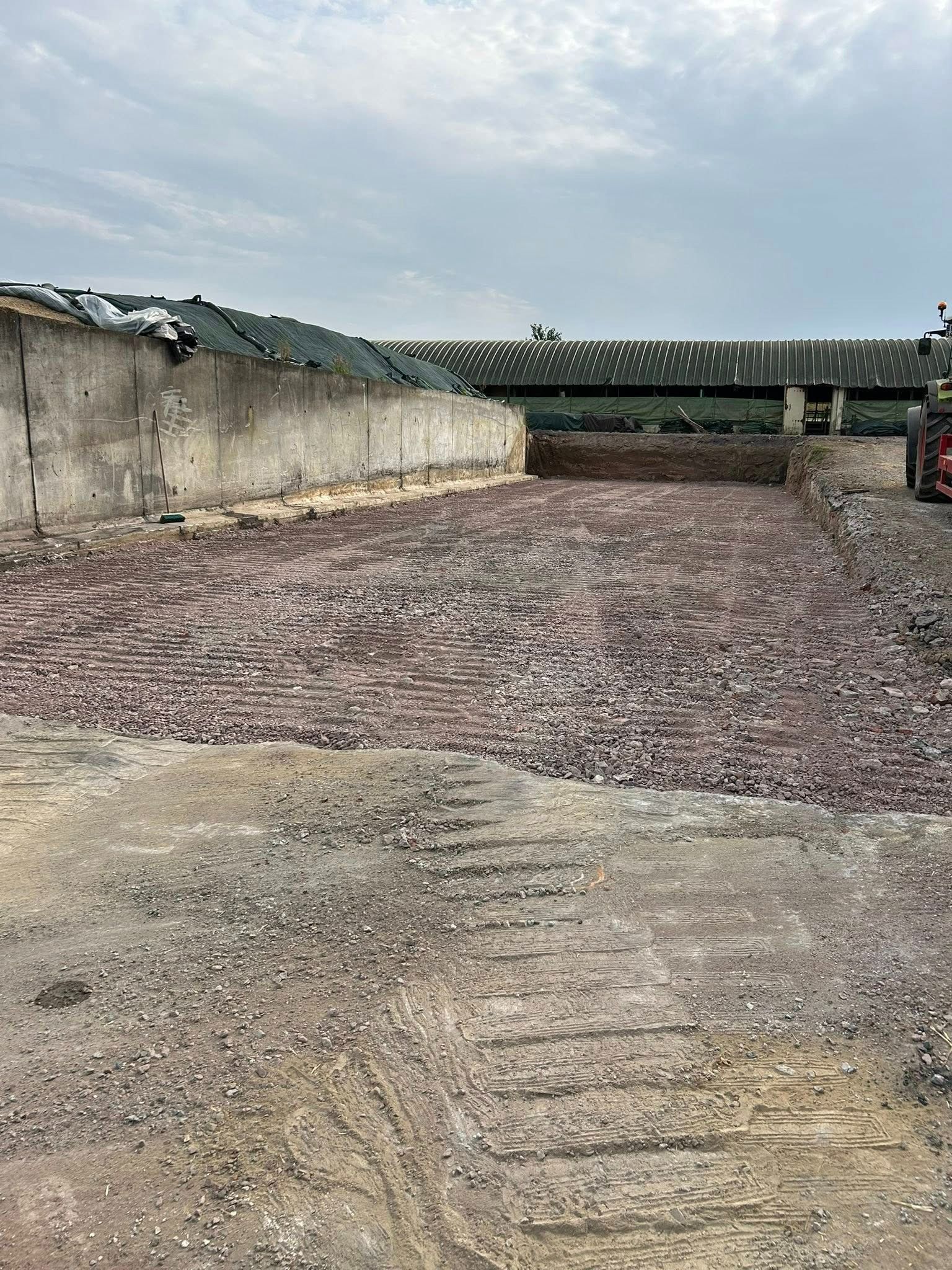 Chantier de construction jonché de débris, avec des fondations en briques apparentes, des murs gris et un ciel nuageux.