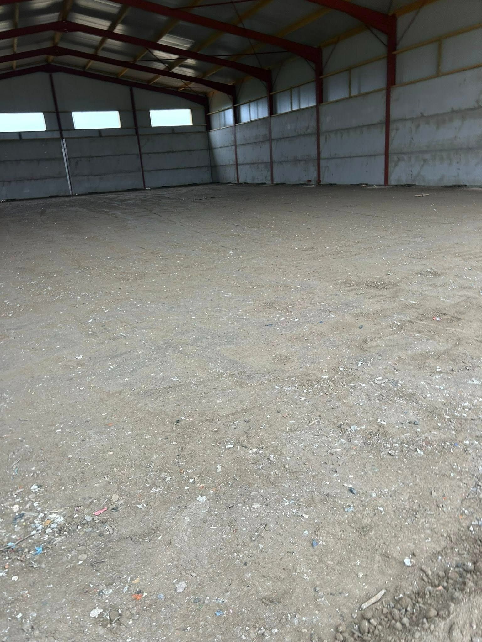 Intérieur d'entrepôt vide avec murs en béton, sol en terre battue et charpente métallique.