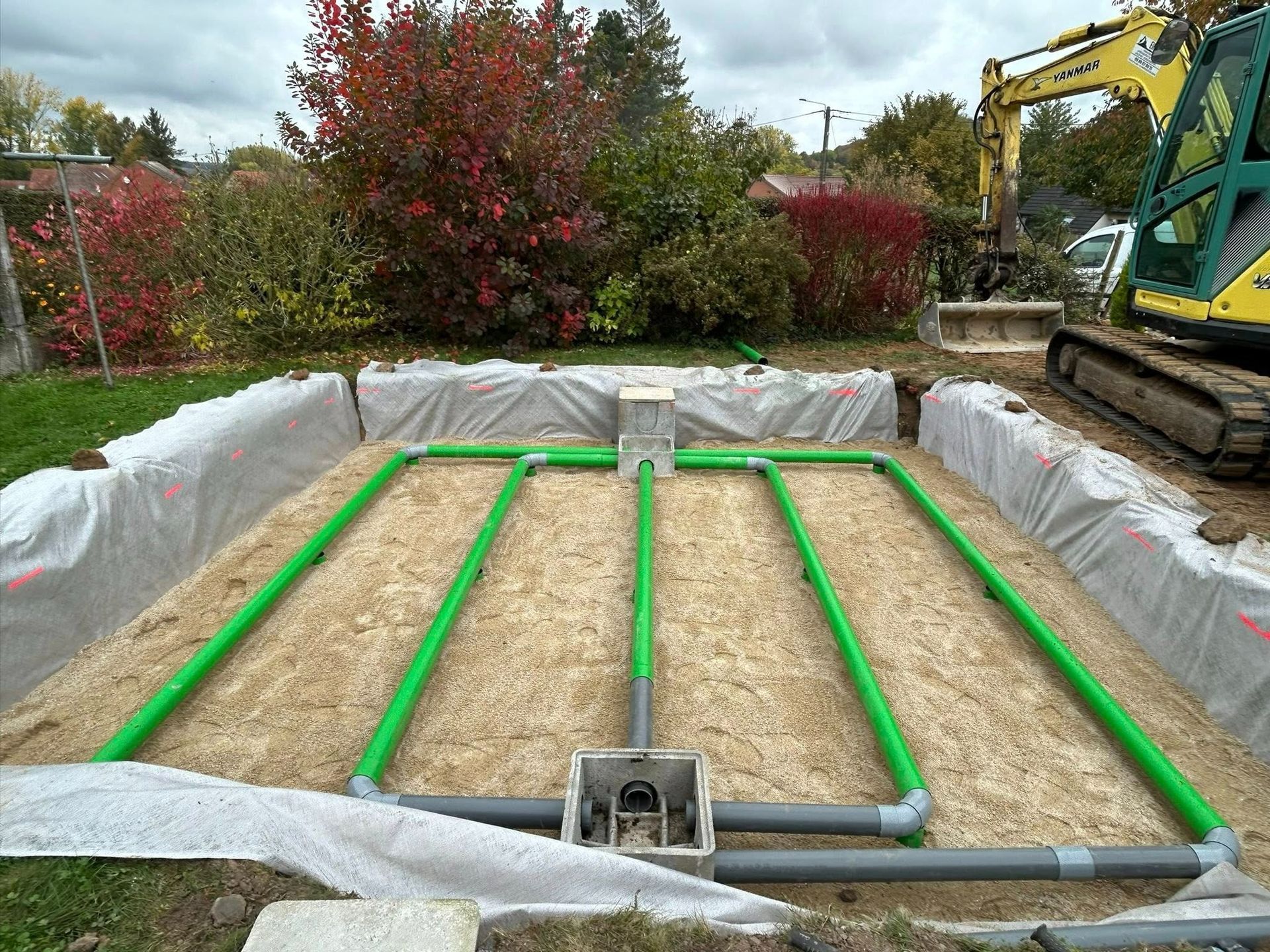 Installation d'une fosse septique : tuyaux verts posés dans une tranchée, reliés à un boîtier de commande central.