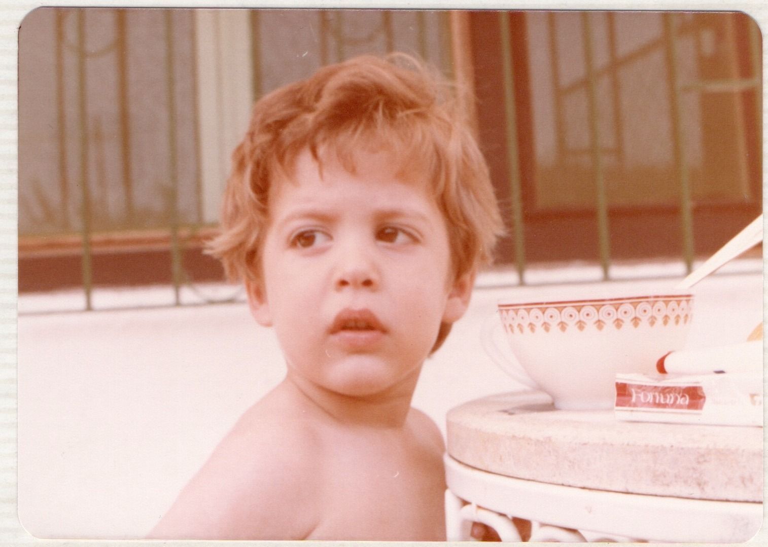 Un niño pequeño con cabello rojo está de pie junto a un recipiente con pasta de dientes.
